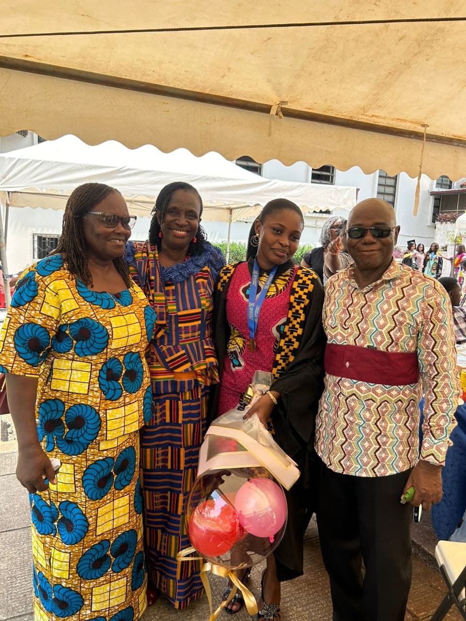 Ebenezer with family at a celebration, holding flowers and balloons